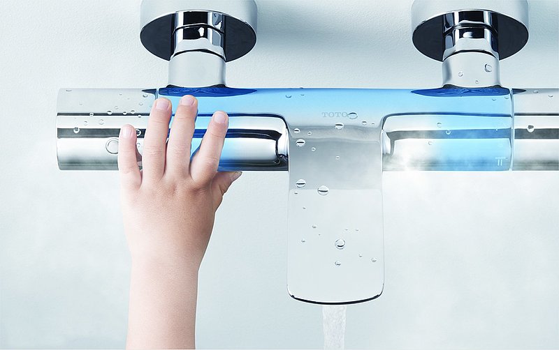 A child grasps a shower fitting with two inlets. The area around the outlet and the inlets is marked in blue. 